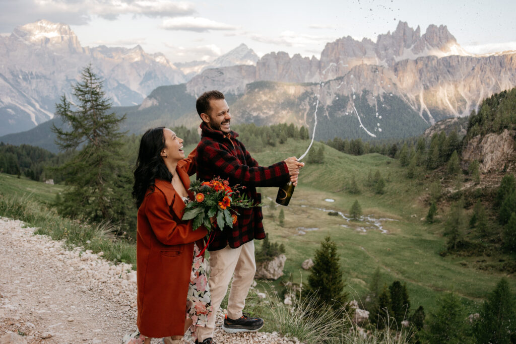 Couple celebrating with champagne in mountain landscape.