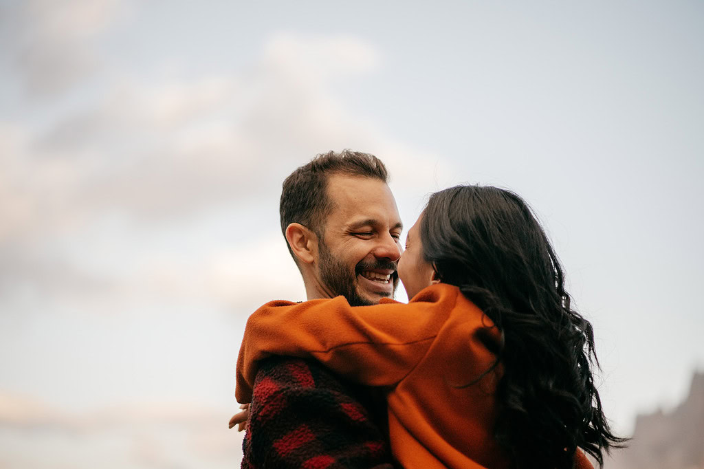 Smiling couple embracing outdoors under cloudy sky.