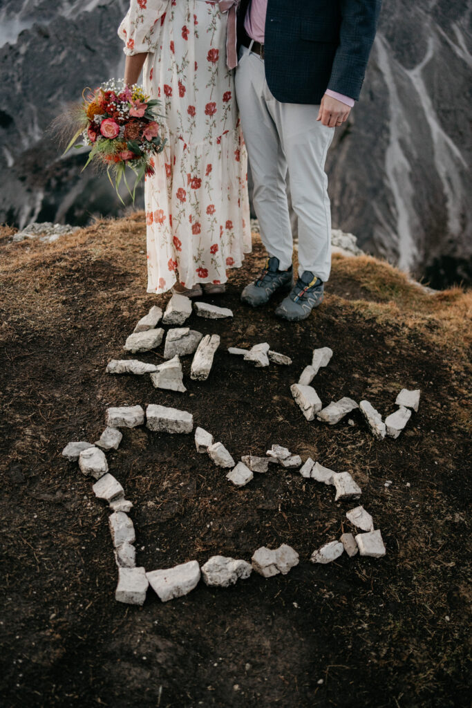 Couple stands on mountain with heart-shaped rocks.