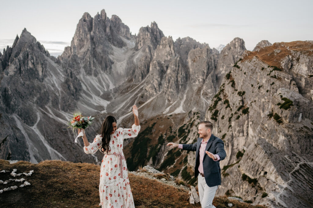 Couple dancing in mountains with bouquet, scenic view.