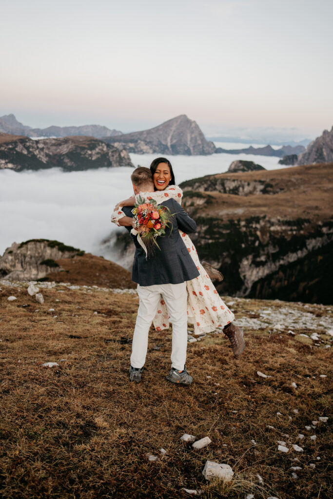 Couple hugging on mountain with bouquet and fog.