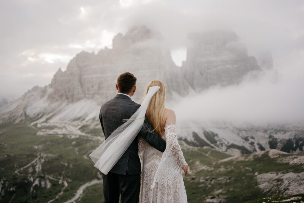 Bride and groom embrace in foggy mountain landscape.