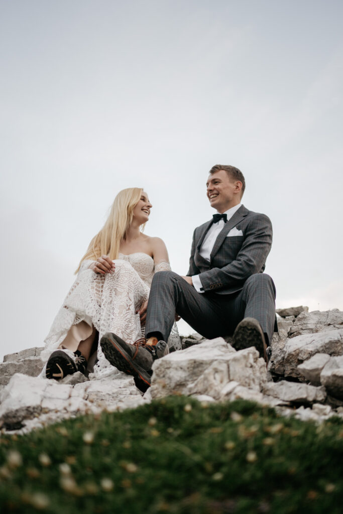 Couple sitting on rocks, smiling at each other.