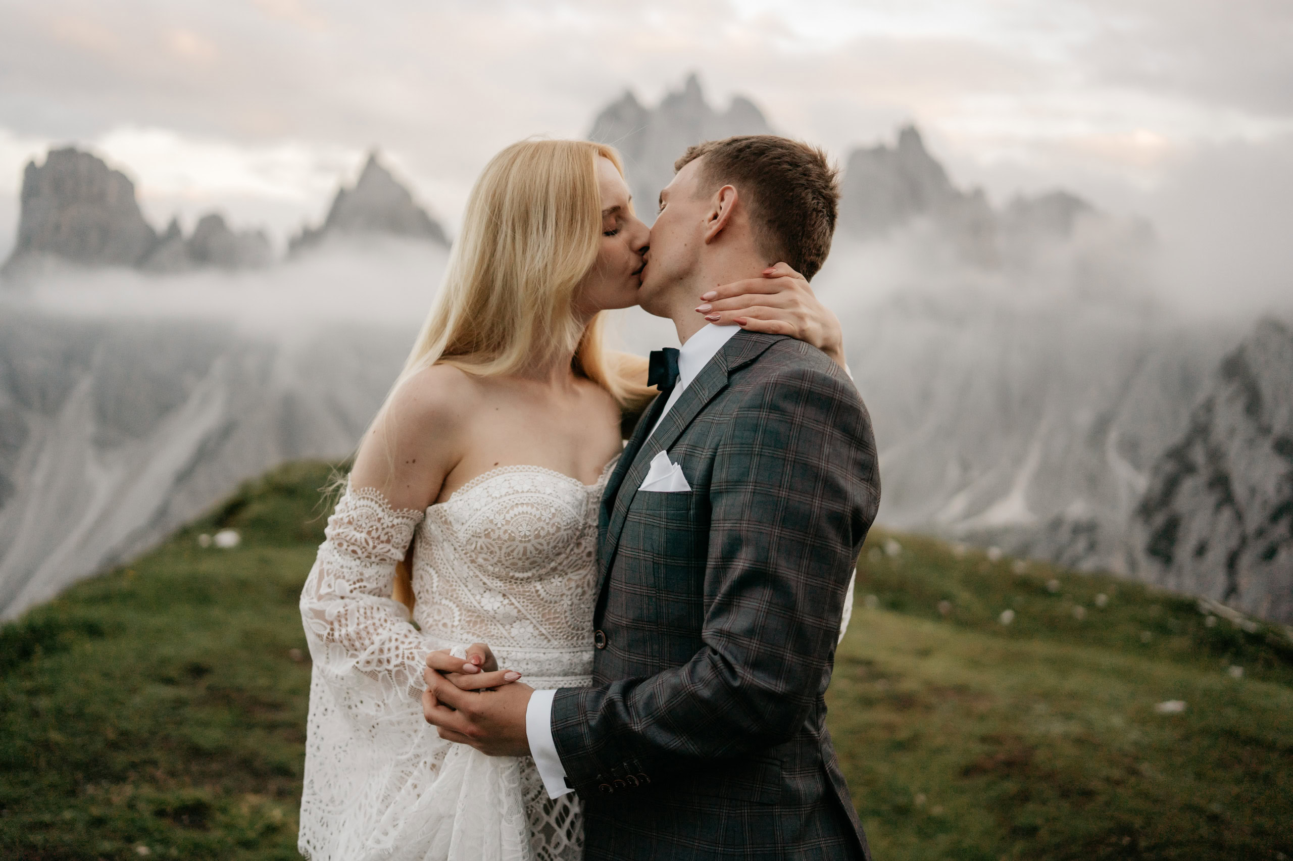 Couple kissing in mountains with cloudy backdrop.