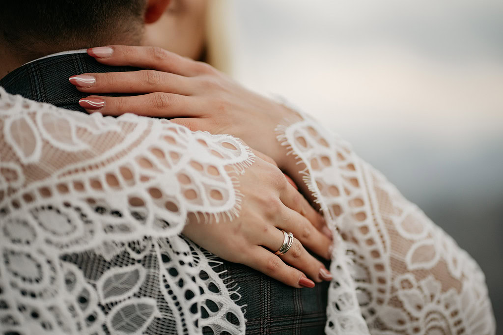 Hands embracing with lace sleeves and wedding rings.