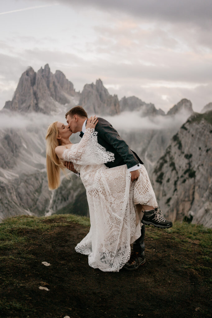 Couple kissing on mountain with misty backdrop.