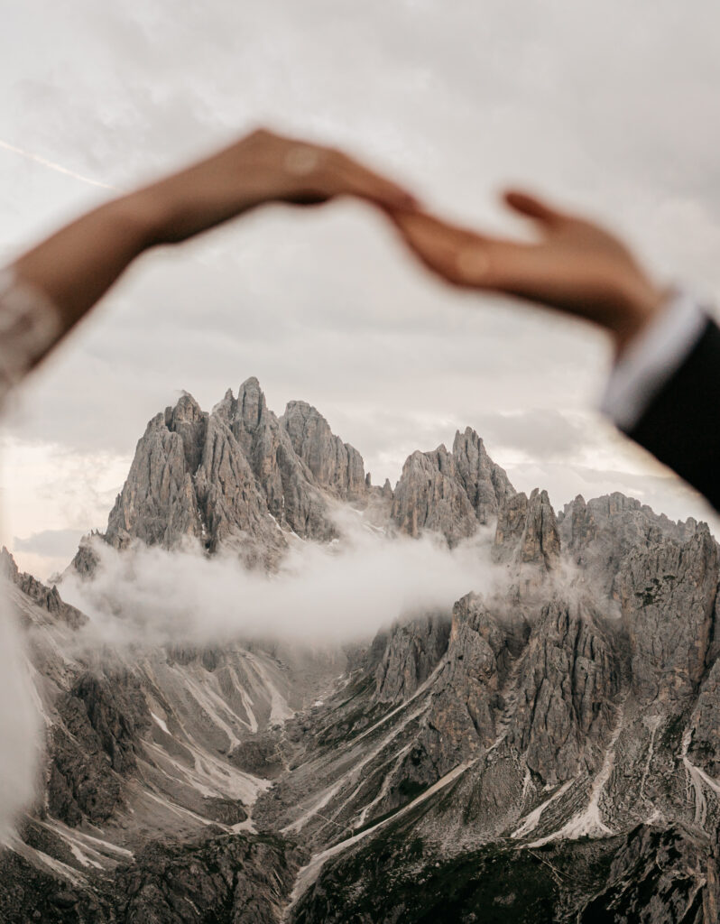 Hands framing scenic mountain view with clouds.