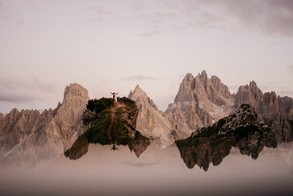 Person stands on mountain with mist and peaks.