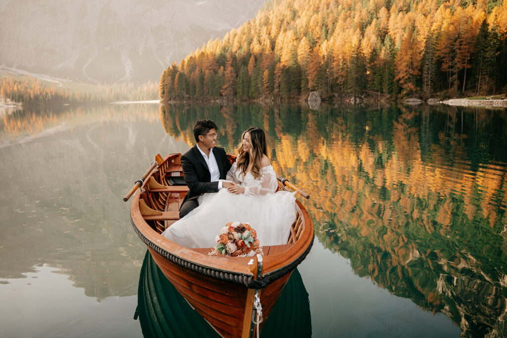 Couple in boat on serene lake with autumn trees.