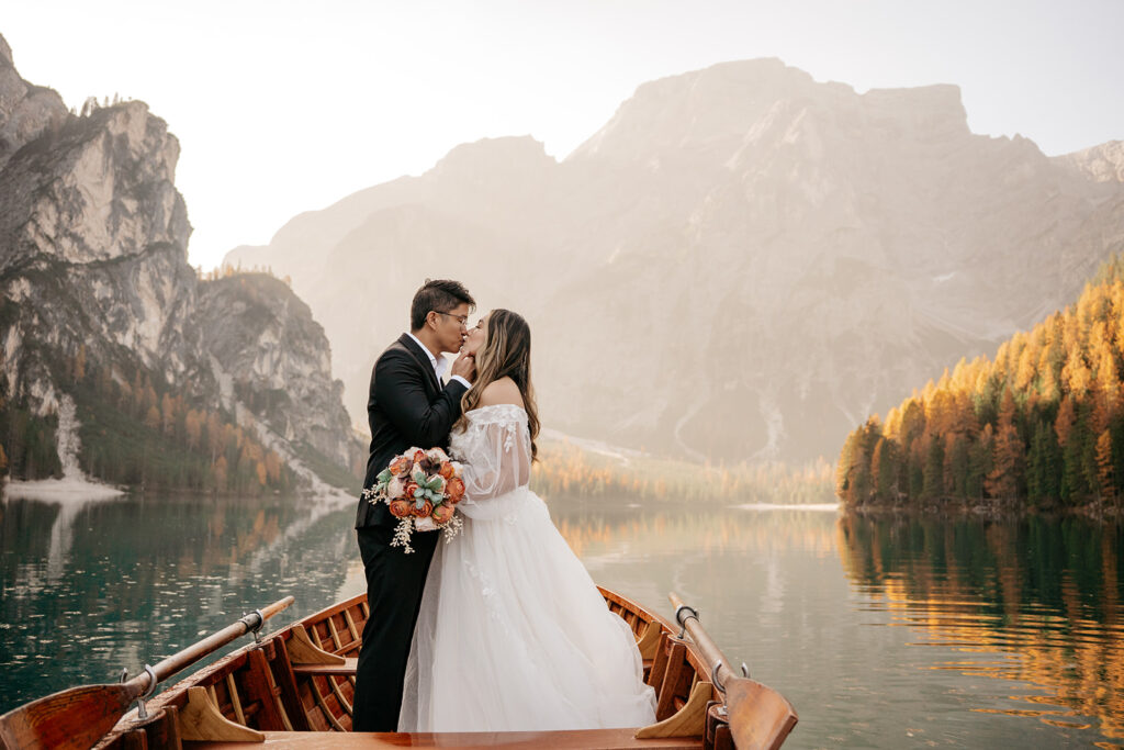 Couple kissing on boat, scenic mountain backdrop.