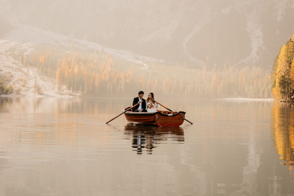 Couple rowing boat on calm lake, foggy autumn scenery.