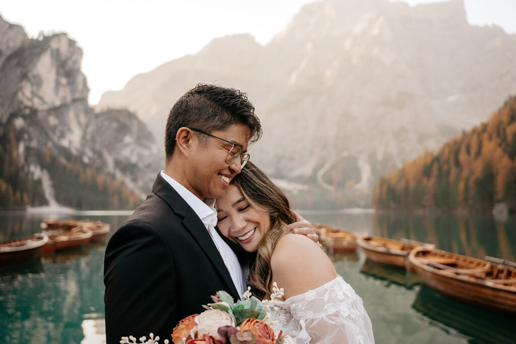 Couple embraces by mountain lake with boats.