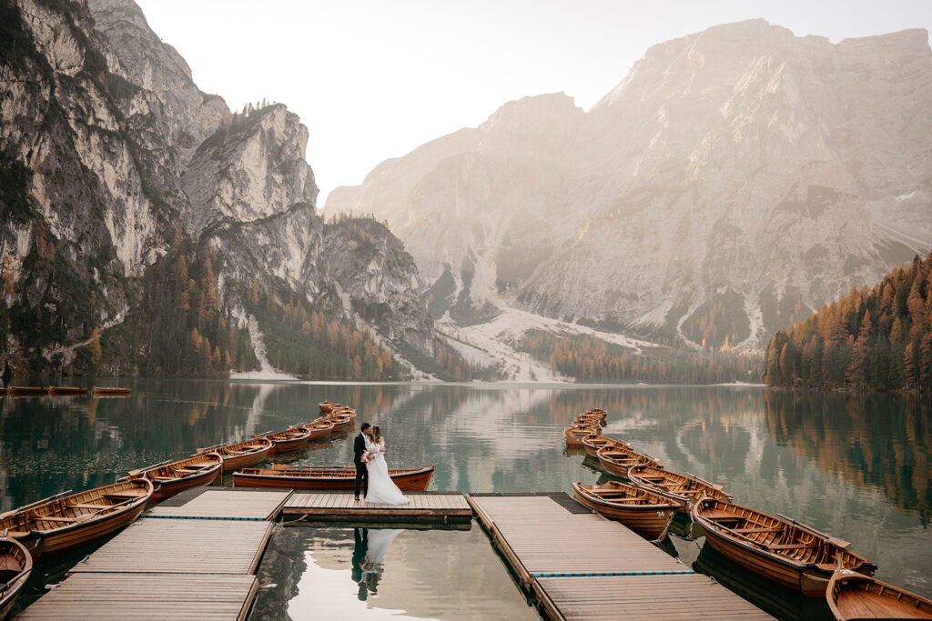 Couple on dock, surrounded by boats, mountain backdrop.