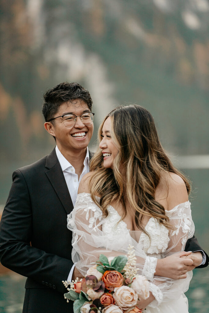 Couple smiling on their wedding day holding flowers.