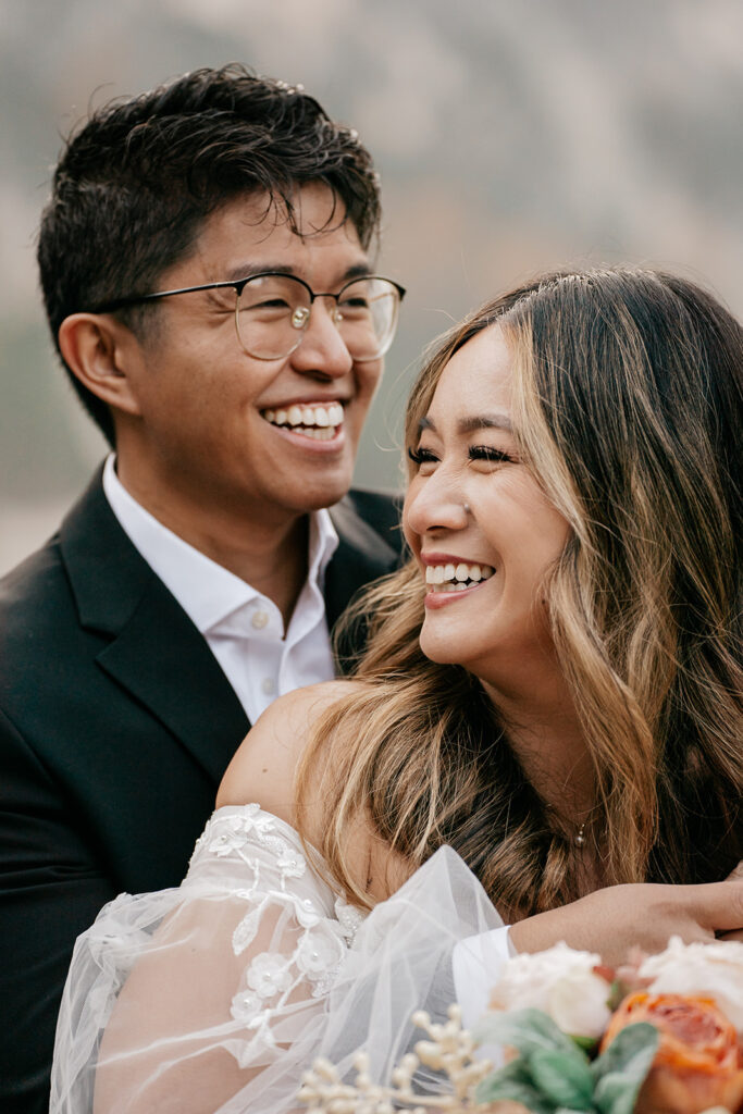 Smiling couple embracing, wedding attire, outdoor setting.