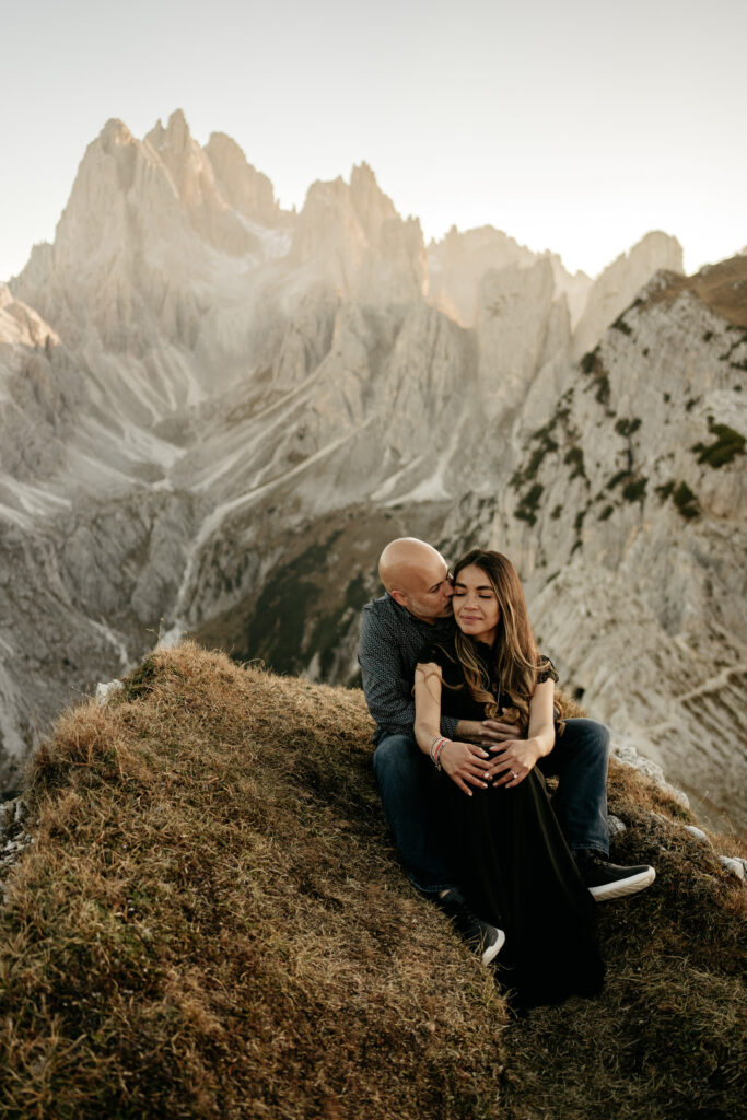 Couple embraces on mountain with rocky peaks background.