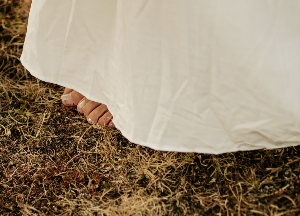 Bare feet under white dress on grass