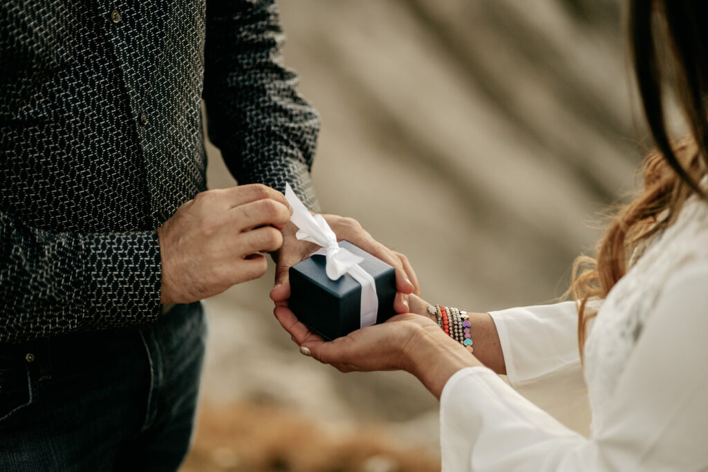 Hands exchanging a small gift box with ribbon.