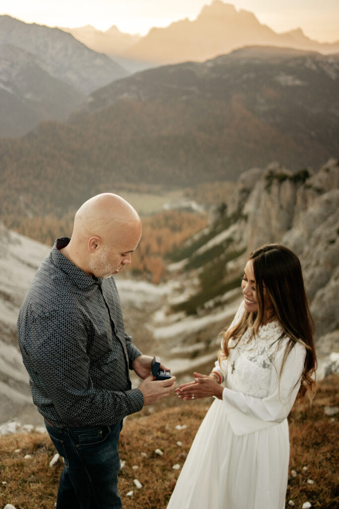 Couple engaged on scenic mountain during sunset proposal.