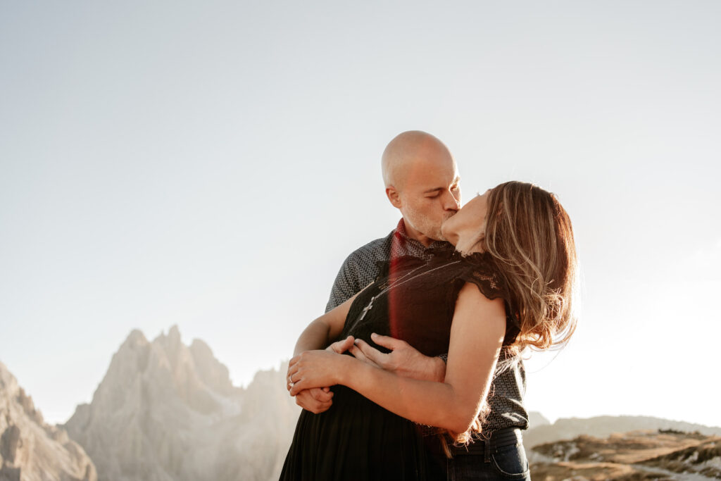 Couple kissing in mountainous landscape at sunset.