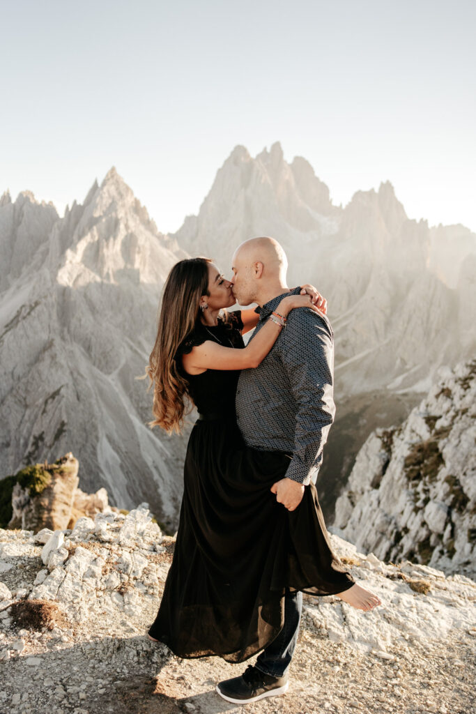 Couple kissing on mountain with scenic backdrop.