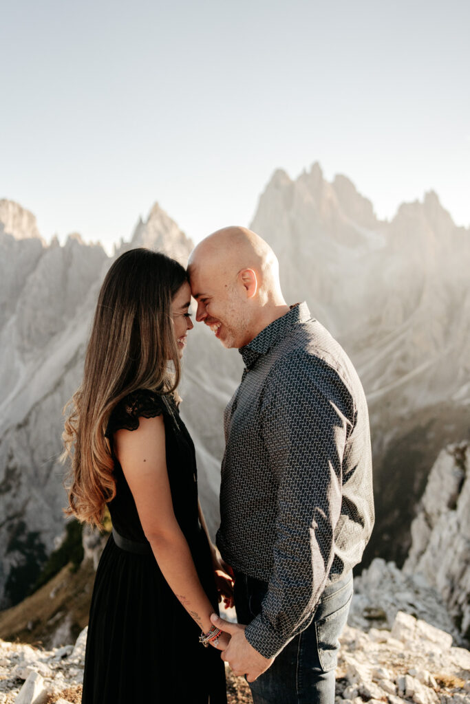 Couple smiling on mountain, touching foreheads.