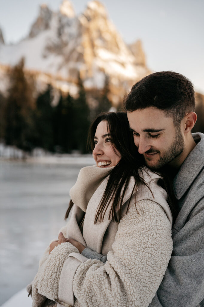 Couple hugging outdoors near snowy mountains.