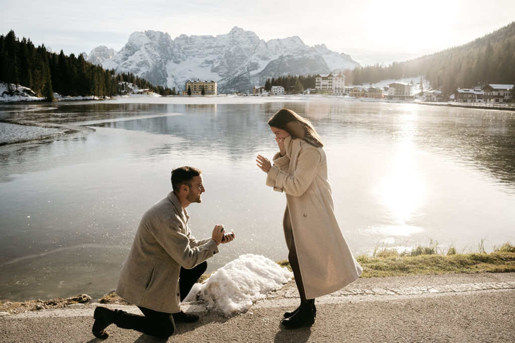 Man proposes to woman by lakeside in mountains.