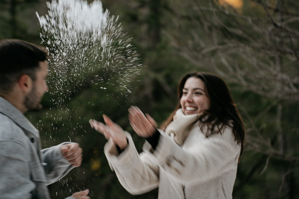 Couple playing with snow outdoors, smiling joyfully.