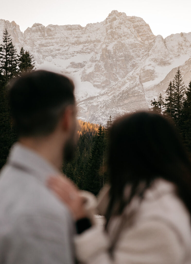 Couple admiring snowy mountain landscape in forest.