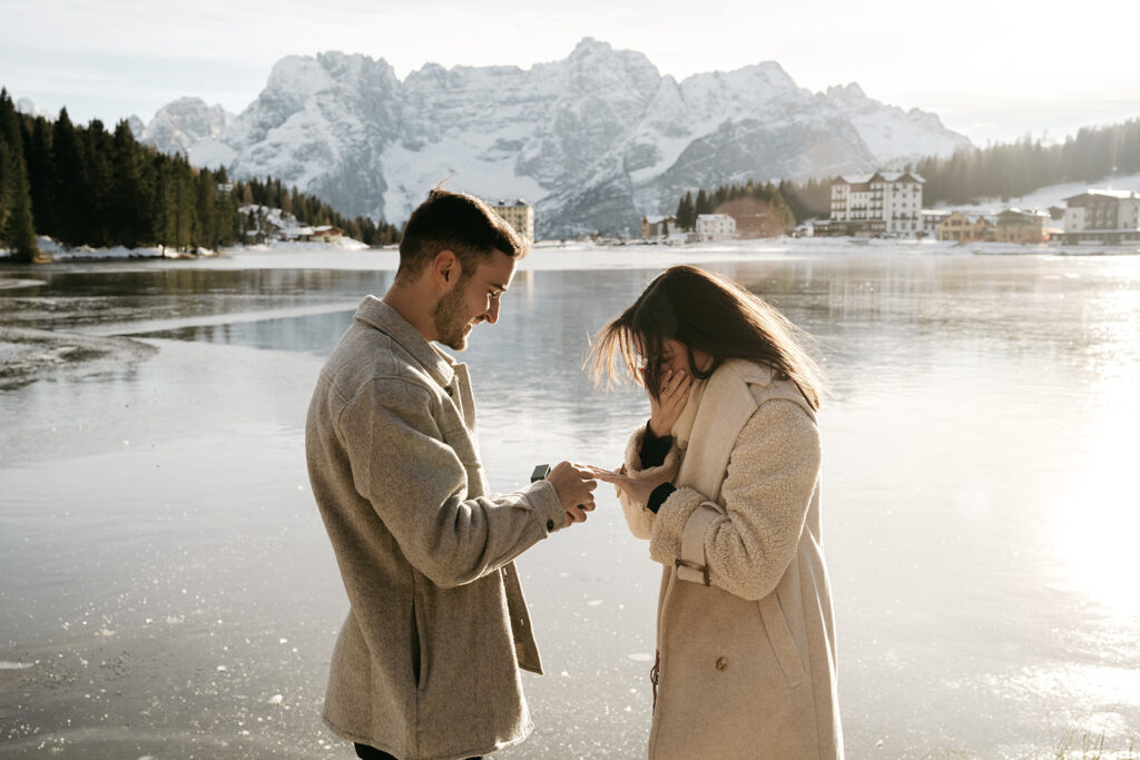 Man proposing by snowy lake, woman surprised