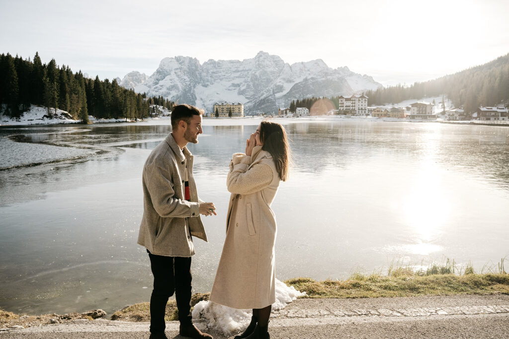 Couple smiling by a snowy mountain lake.