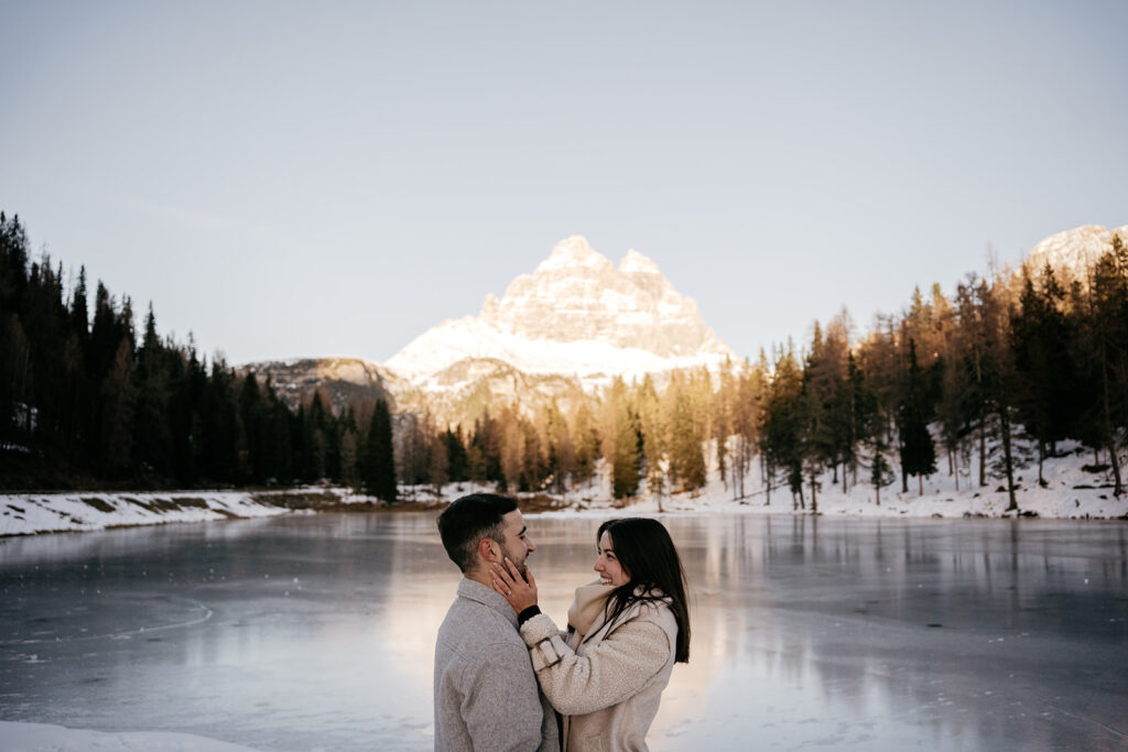 Couple embraces by a snowy mountain lake.