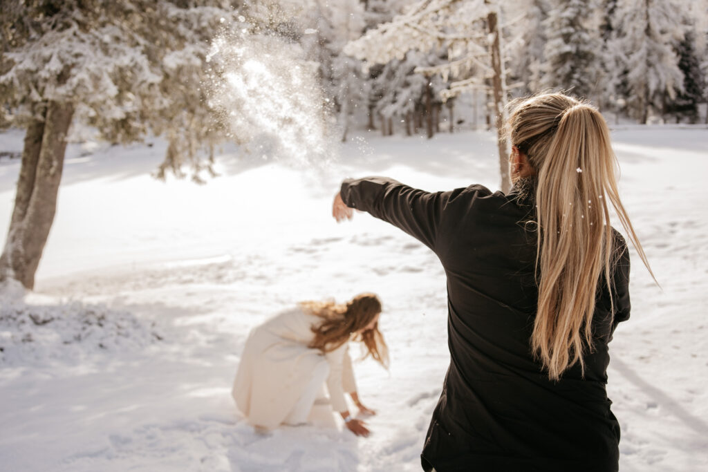 Woman playfully throwing snow at friend in winter forest.