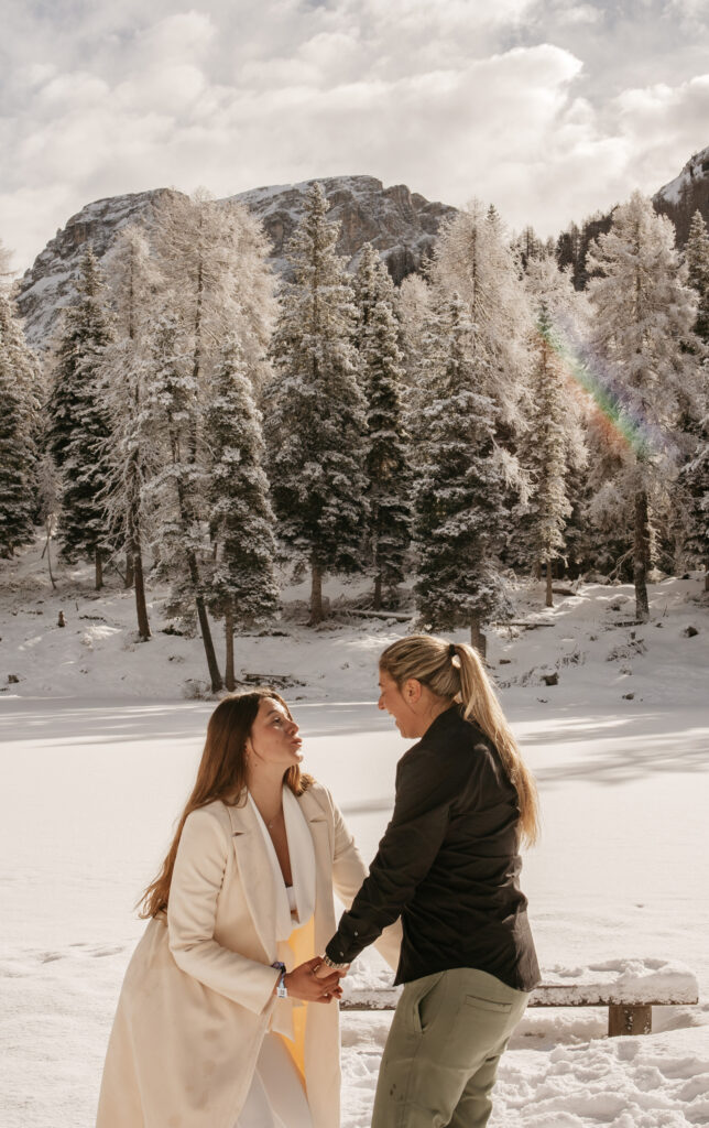 Two people smiling in snowy forest landscape.