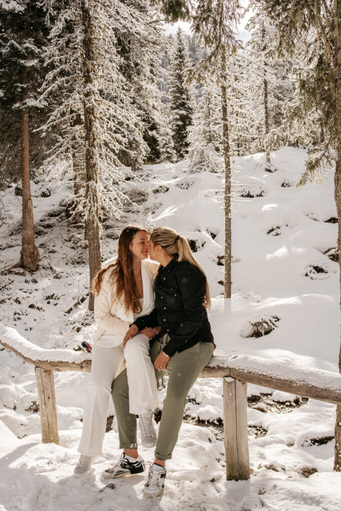 Couple sitting on snow-covered bridge in forest.