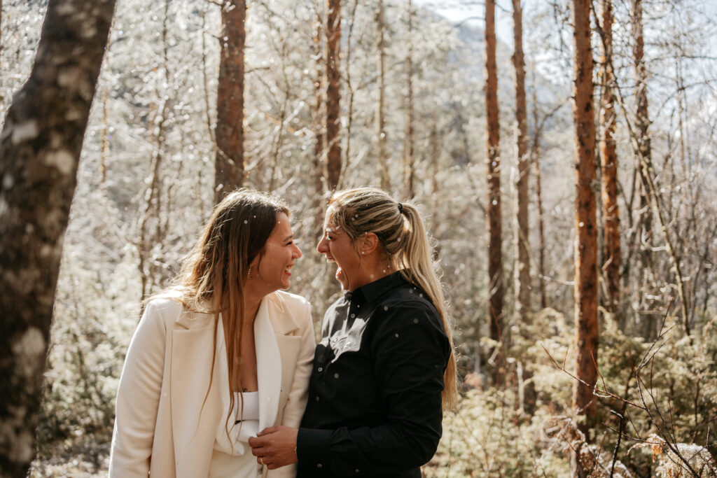 Two women laughing in a snowy forest.