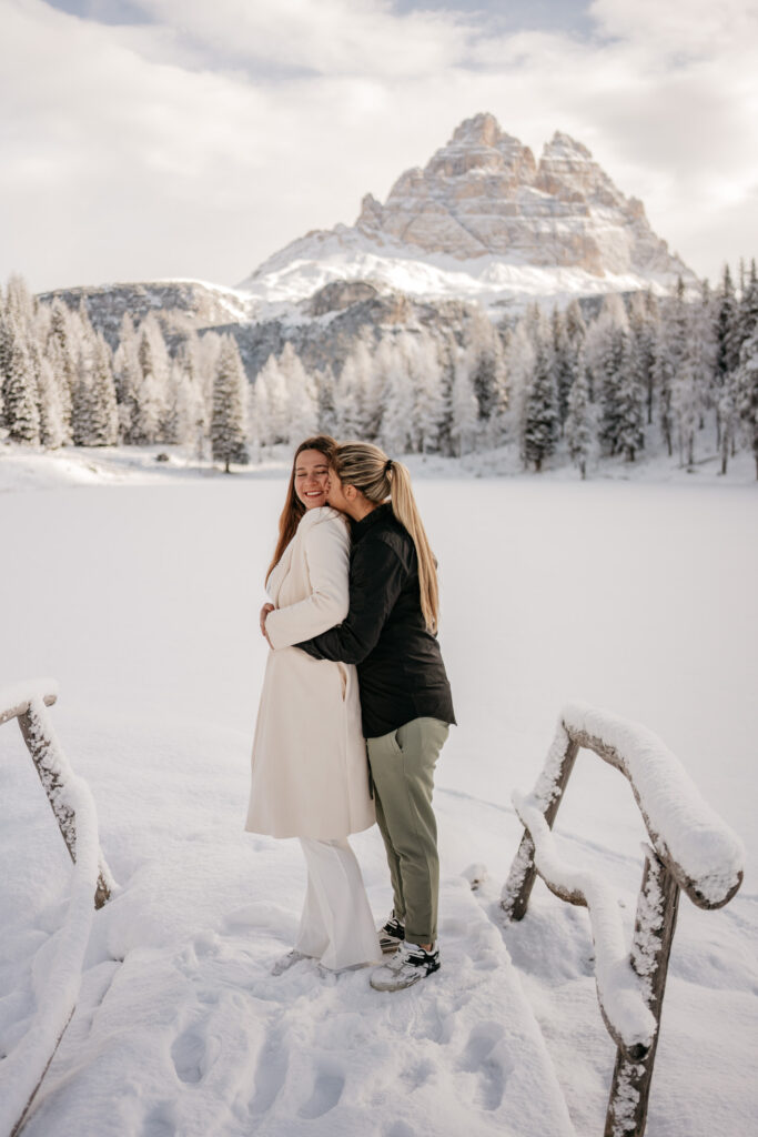 Couple embraces in snowy mountain landscape.