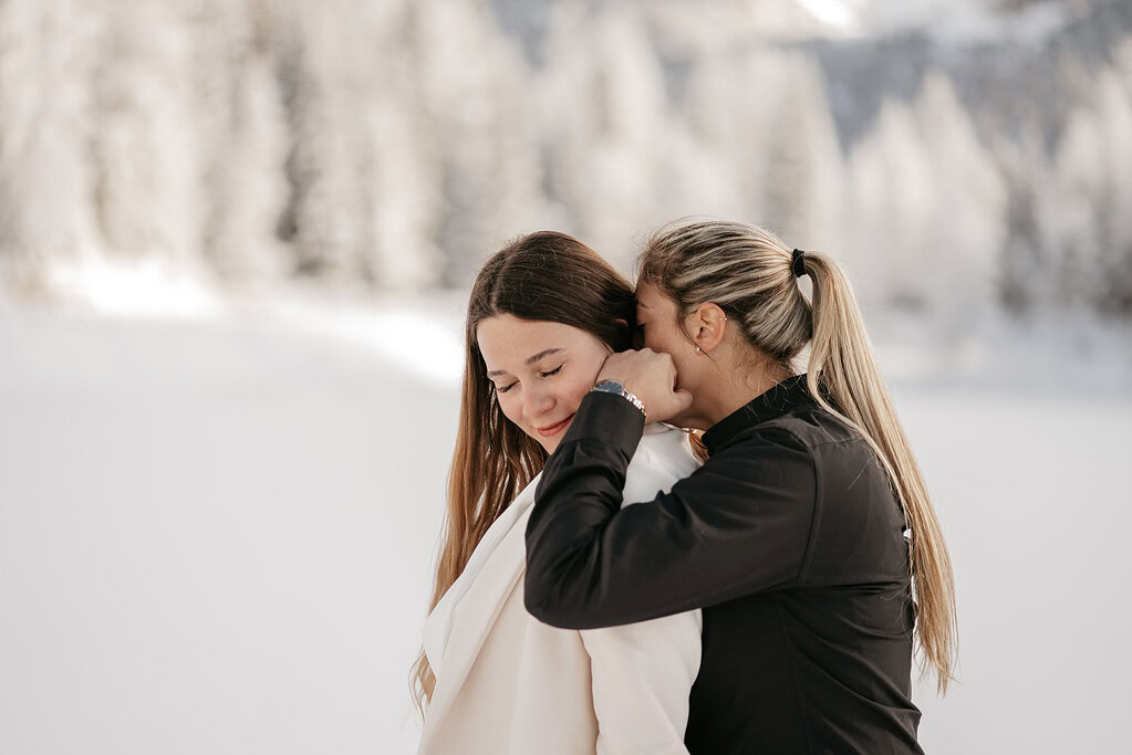 Two women hugging in snowy landscape.