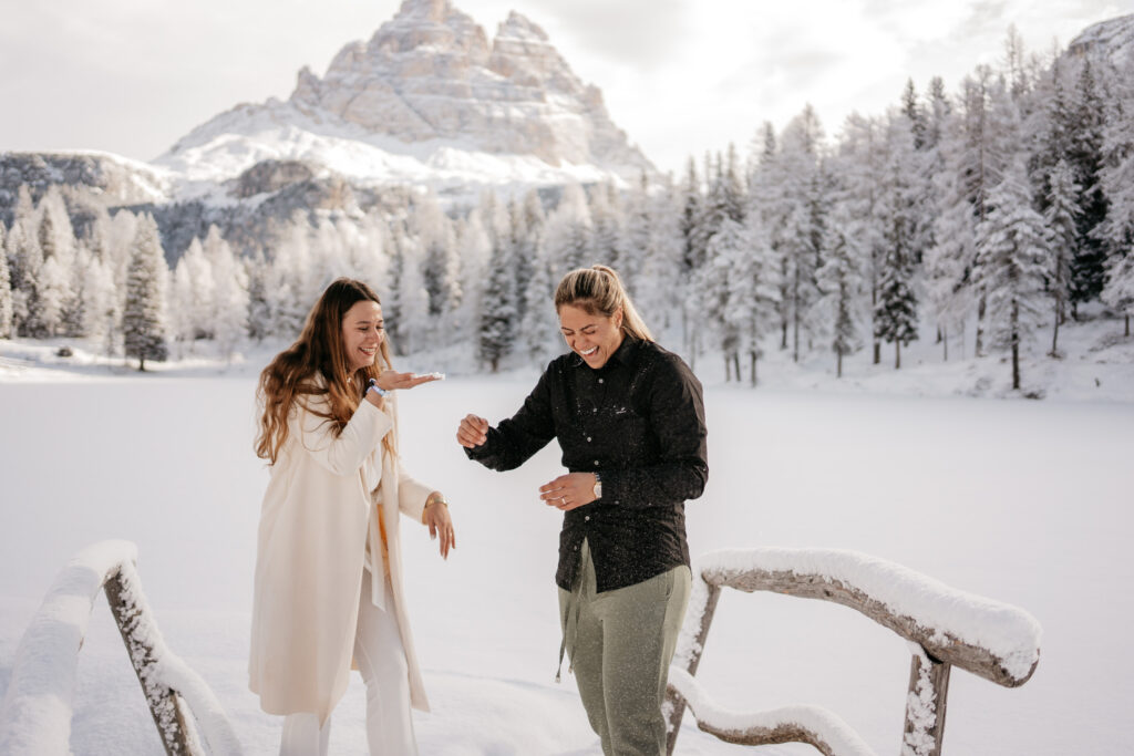 Two women laughing in snowy mountain landscape.