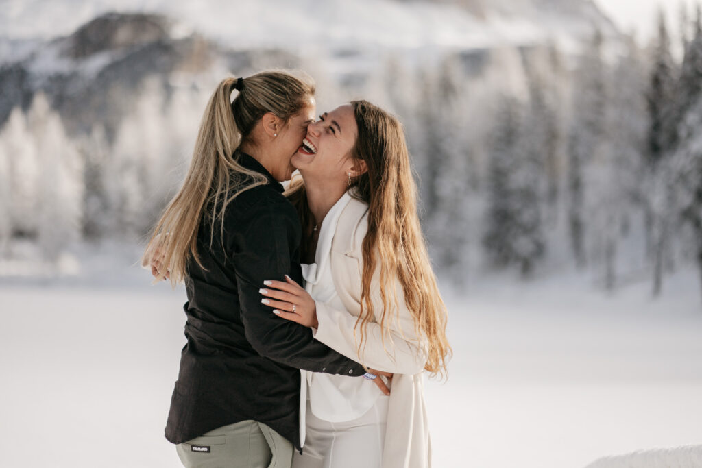 Two women laughing in snowy landscape.