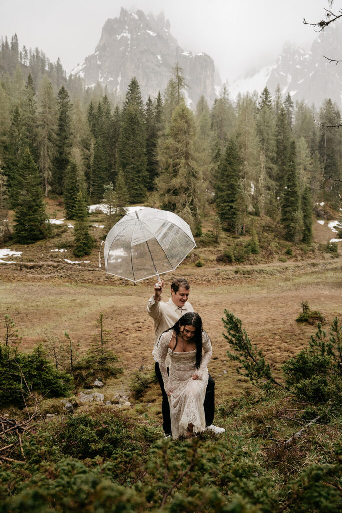 Couple hiking in forest with umbrella in rain.