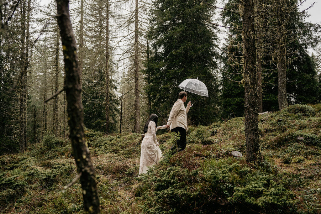 Couple walking in forest holding umbrella.