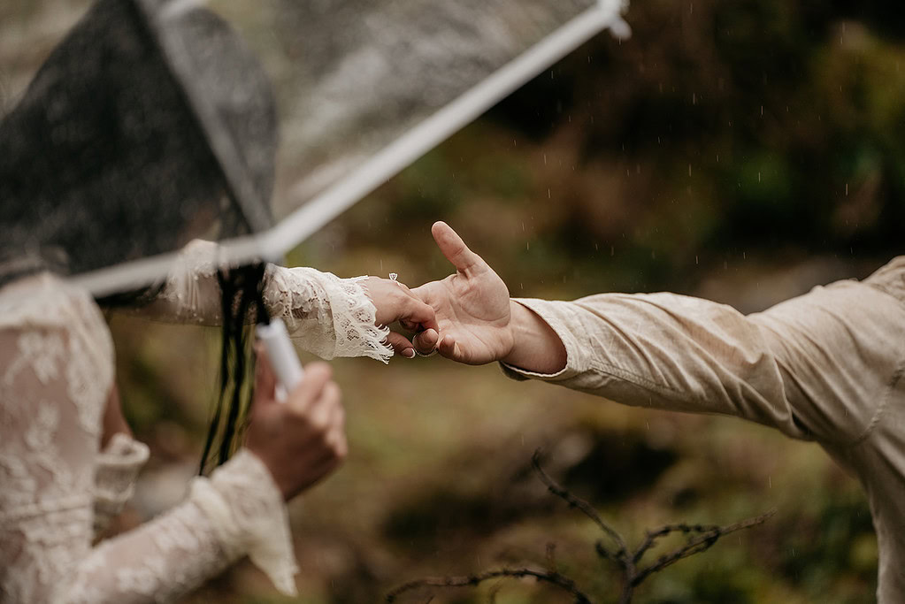 Hands reaching under lace umbrella in the rain.