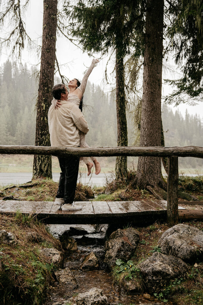 Couple embracing on forest bridge, joyful moment captured.