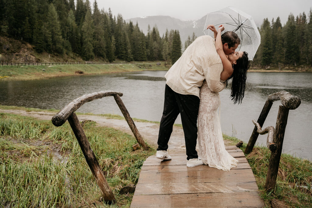 Couple kissing on rainy bridge with umbrella.