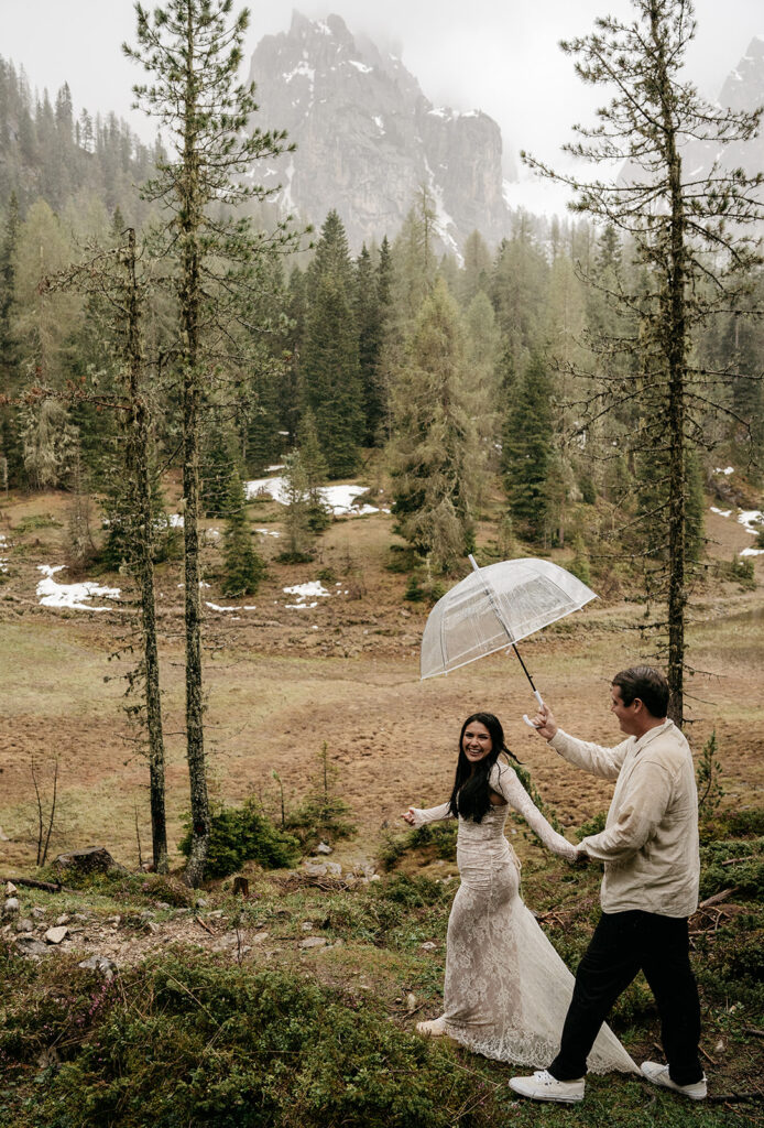 Couple holding umbrella in forest with mountains.