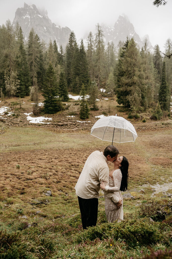 Couple kissing under umbrella in mountain meadow