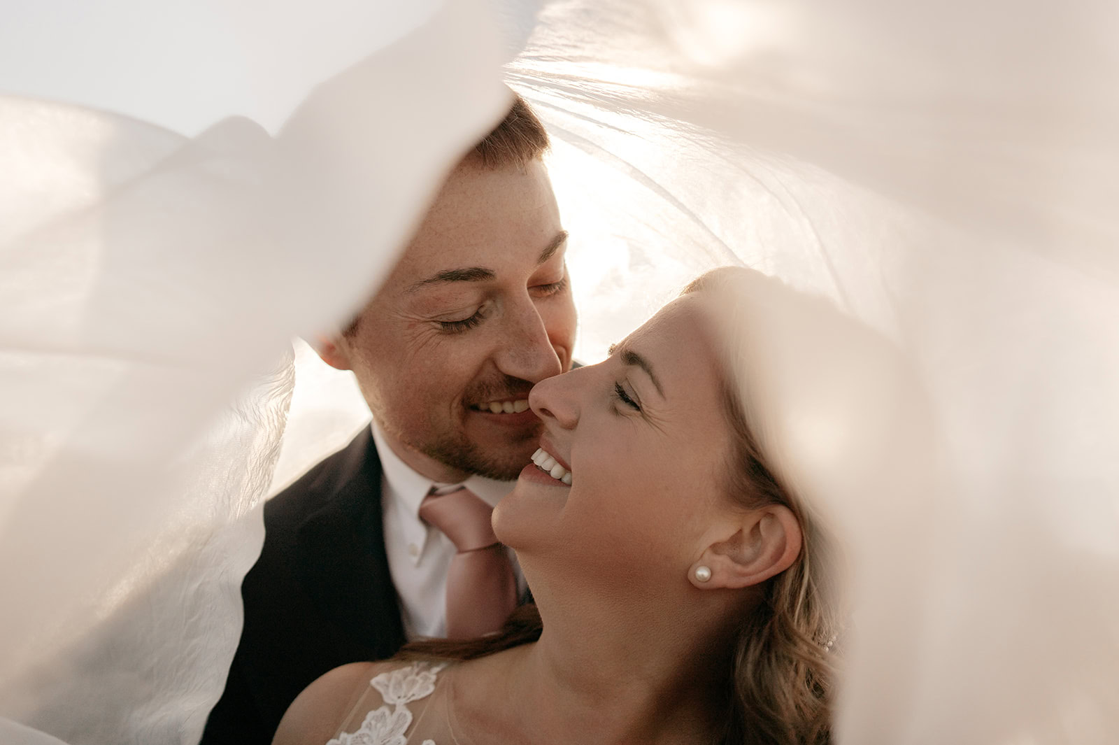 Couple smiling under wedding veil.