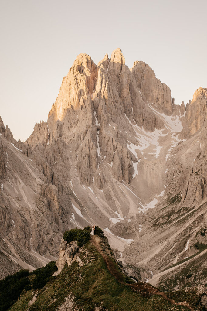 Couple on mountain ridge with snowy peaks.